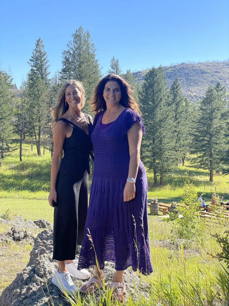 Five Stars Around The Sun Founders Laura and Athanasia stand together in a field with mountains in the background.